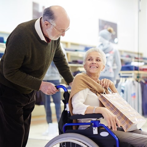 husband pushes wife in wheelchair while shopping